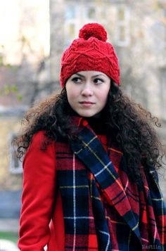 a woman with curly hair wearing a red hat and plaid scarf is looking at the camera