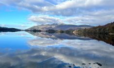 the mountains are reflected in the still water on the lake's edge, while clouds loom overhead