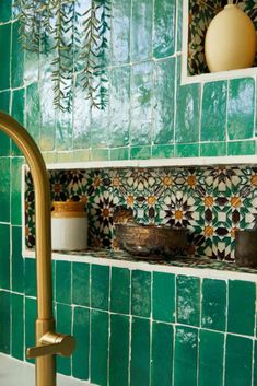 a green tiled bathroom with gold faucet, sink and shelf above the bathtub