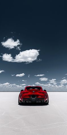 a red sports car is parked in the middle of an empty parking lot under a cloudy sky