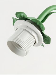 a green and white light fixture on a white wall with leaves coming out of it