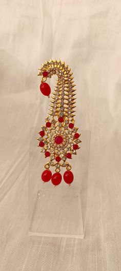 a pair of red and gold earrings on a clear acrylic stand with white background