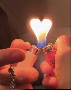 someone holding two lighters in their hands with a heart shaped light on the top