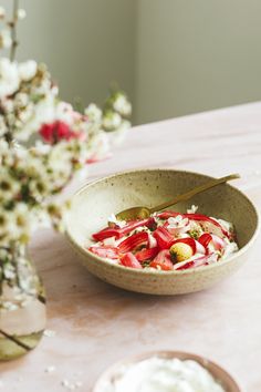 a bowl of strawberries and whipped cream sits on a table next to a vase with flowers