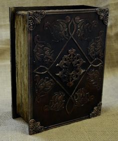 an old book with ornate designs on it sitting on a cloth covered tableclothed surface