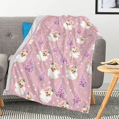 a pink blanket with white poodles and snowflakes on it is sitting next to a gray couch