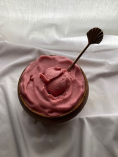 a cupcake with pink icing and a spoon in it on a white cloth