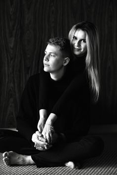 a man and woman sitting on the floor with their arms around each other, posing for a black and white photo