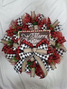 a red and black christmas wreath with merry lettering on the front, sitting on a white sheet