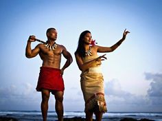 a man and woman dressed in native american clothing standing on the beach next to the ocean