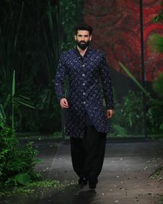 a man walking down a runway wearing a blue and black suit with an intricate pattern on it