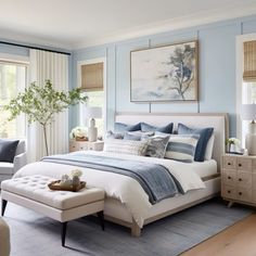 a bedroom with blue walls and white bedding, two windows, an ottoman, and a painting on the wall