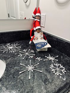 an elf is sitting on top of a box in the bathroom with snowflakes