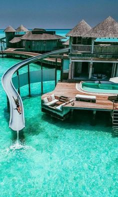 a water slide in the middle of some clear blue water next to an overwater resort