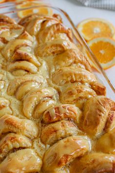 a glass baking dish filled with oranges and cinnamon rolls covered in icing next to sliced orange slices