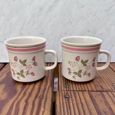 two coffee mugs sitting on top of a wooden table next to each other with flowers painted on them