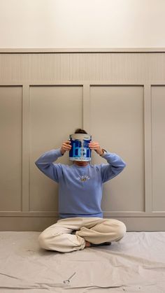 a person sitting on the ground holding up a cup in front of their face with both hands