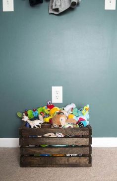 a wooden crate filled with stuffed animals on top of carpeted floor next to wall