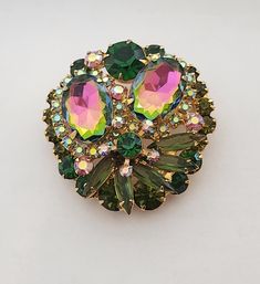 Stunning Juliana also known by name DeLizza & Elster Brooch in very good pre-loved condition.  Measures 1 3/4" in diameter. Brooch is featuring  two larger watermelon rhinestones (they mix of green and pink colors)  dark green,  olivine, pink  and Aurora Bareilles rhinestones. Brooch is identified for being Juliana by construction and setting of the stones. The original was sold with paper hang tag was used on jewelry and most likely was discarded by original owner.  Juliana jewelry was named after Frank DeLizza mother.  This style was always carried by DeLizza & Elster. Highly collectable.  Perfect for any occasion. Juliana Jewelry, Vintage Rhinestone Jewelry, Green And Pink, Rhinestone Jewelry, Rhinestone Brooches, Vintage Rhinestone, Antique Jewelry, Halloween Shopping, Pink Color