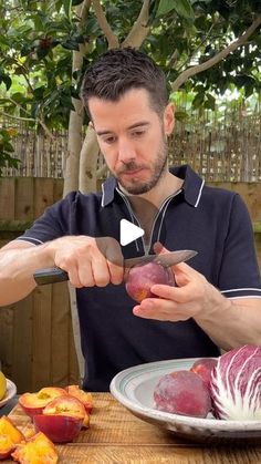 a man cutting up some fruit on top of a wooden table in front of a tree