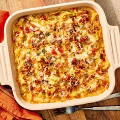 a casserole dish with cheese and vegetables in it on a wooden table next to utensils