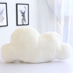 a white cloud pillow sitting on top of a table next to two framed pictures in the background