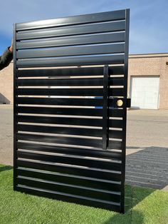 a man standing next to a black metal door on top of green grass covered ground