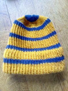 a yellow and blue striped knitted hat sitting on top of a wooden table next to a pair of scissors