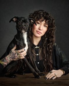 a woman sitting at a table with a dog in her lap and tattoos on her arm