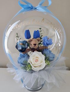 a clear glass ball with blue flowers and a teddy bear in it on a table