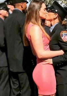 two police officers are kissing each other in front of some uniformed men and women at an outdoor event