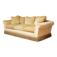 a beige couch with pillows and fringe trim on the arm rests against a white background