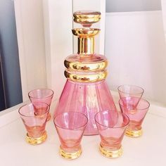 a pink vase with gold trim and four glasses