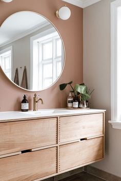 a bathroom with a large round mirror on the wall and wooden cabinets in front of it