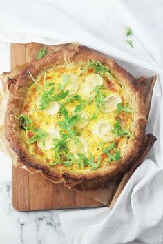 a quiche with cheese and greens on a wooden cutting board next to napkins