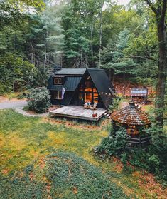 a small black cabin in the woods surrounded by trees and grass with people sitting outside