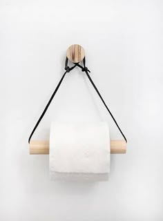 a white toilet paper roll hanging from a wooden holder with black string on the wall