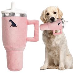 a dog is holding a toy in its mouth while sitting next to a coffee mug