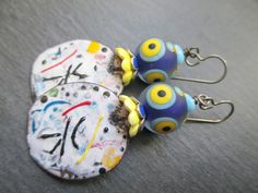 These fun earrings use abstract enameled copper charms by the madly talented Andrea of JosephineBeads in Utah. The circular charms are white with vibrant lines and dots in black, yellow, blue and red. They have the feeling of a shower of confetti after a big celebration. Above the colorful charms are yellow ceramic flower bead caps followed by nay and silver enameled flower bead caps. The hold wonderfully whimsical lamp-work glass beads by Unventdeliberte in France. The matte lamp-work glass bea Whimsical Lamp, Lines And Dots, Dichroic Glass Earrings, Lampwork Earring, Abstract Earrings, Soldering Jewelry, Yellow Ceramics, Funky Earrings, Art Earrings