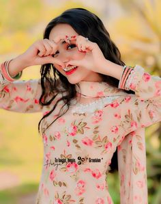 a woman with long black hair wearing a pink floral dress and holding her hands up to her face