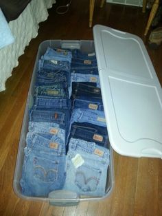 a plastic container filled with lots of blue jean pants on top of a wooden floor