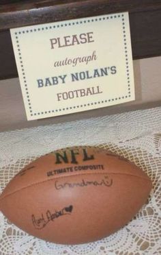 a football sitting on top of a table next to a sign that reads please autograph baby nolan's football