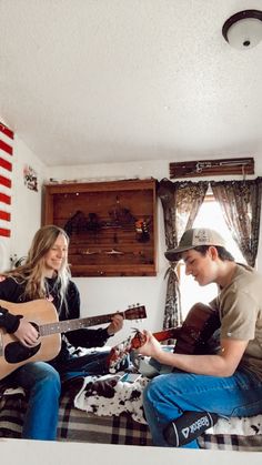 two people are sitting on a bed playing guitars and singing to each other while another plays the guitar