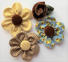 three fabric flower brooches are shown on a white surface, one is brown and the other is blue