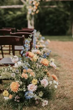 a row of wooden chairs sitting next to each other on top of a grass covered field