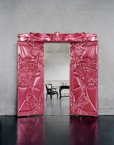 an open pink door with a table and chair in the background on a black floor