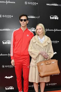 a man and woman standing next to each other in front of a black wall with white lettering on it