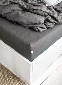 an unmade bed with grey linens on it