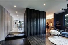 a living room filled with furniture next to a tall black wall on the side of a wooden floor