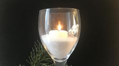 a lit candle in a wine glass filled with water and snowflakes on a black background